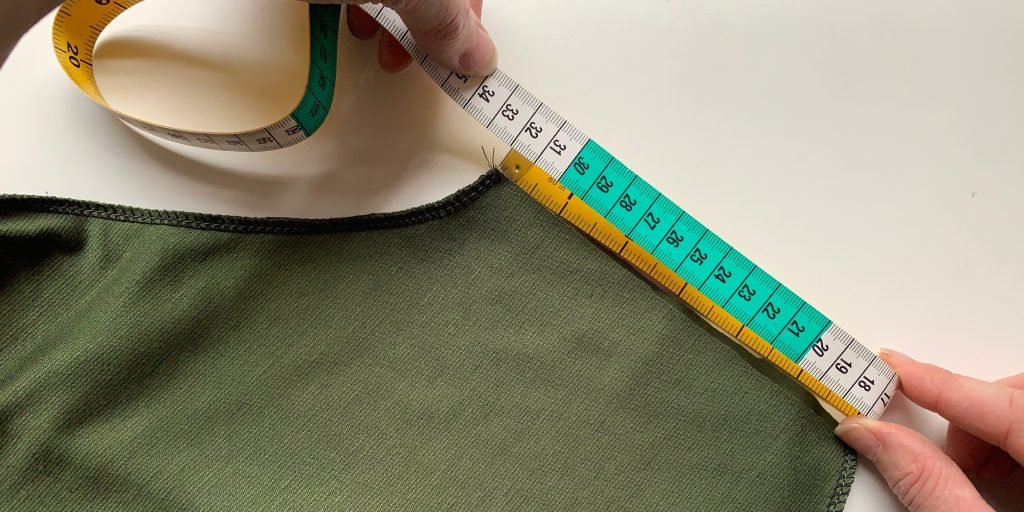 A close up of a tape measure being used against the sleeve end of a green top.