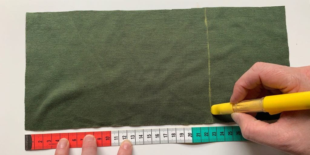 A strip of green fabric being measured with a tape measure and marked with a yellow fabric marker.